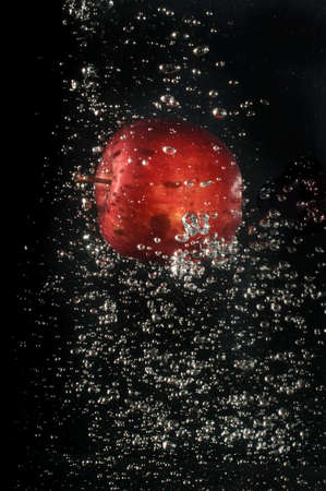 Red apple falling into water on black backgroundの写真素材