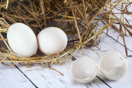 Fresh duck eggs and eggshell with nest of hay on wooden background