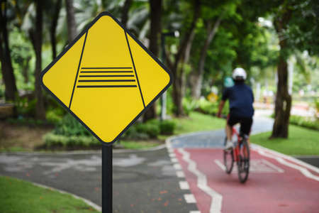 BANGKOK, THAILAND - JULY 2017: Caution slow down rider traffic sign and rider on bike lanes at Benchakitti Park on JULY 10, 2017 in BANGKOK, THAILANDの写真素材