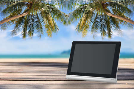 Computer tablet with blank screen on planks on tropical beach backgroundの写真素材