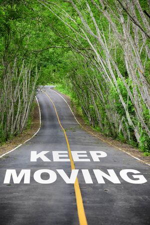 Tree tunnel with keep moving word on asphalt road surface, business success concept and natural ideaの写真素材
