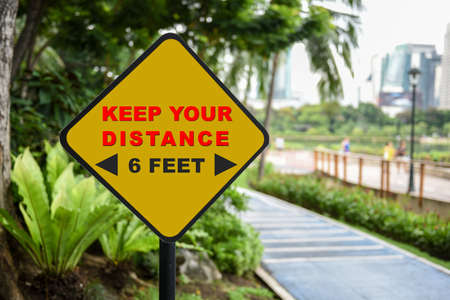 Keep your distance and 6 feet word on yellow sign at park background. Coronavirus disease 2019 or...