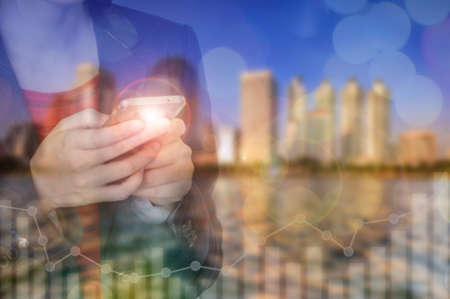 Businesswoman using smart phone on cityscape background. Technology for investment concept and...