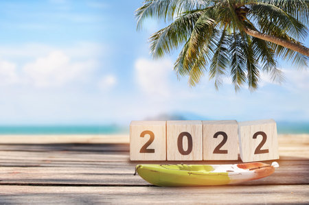 2022 written on wooden cube with boat kayak on planks on tropical beach background, natural...