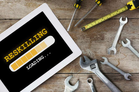 Reskilling loading on digital computer tablet and tools supplies on wooden background. New skills concept and technology transformation learning model ideaの写真素材