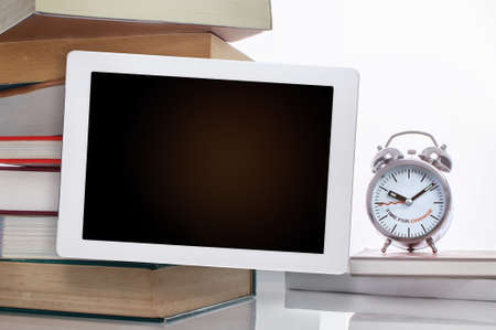 Blank digital computer tablet with stack of textbook with time to change words on alarm clock...