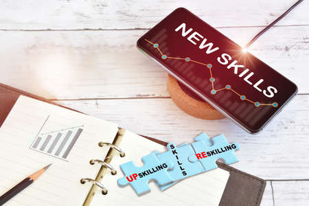 New skills technology on smart phone screen with growth graph on wireless charger with reskilling, up skilling and skills written on blue puzzle on desk. Artificial intelligence machine learning concept and automation ideaの写真素材