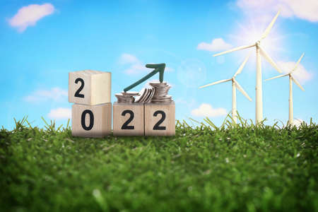 New year 2022 and stack of coins with wind turbine on green grasses on fluffy cloud background....