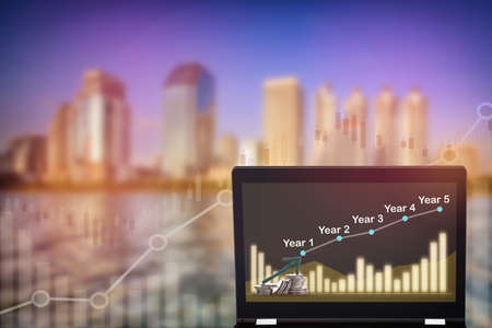Uptrend and bull market trading concept and real estate idea. Stock market trading profit and return on investment on computer laptop on growth graphs on modern business building backgroundの写真素材