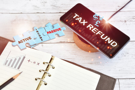 Tax refund concept  and work anywhere idea. Income earning finance technology growth graph on smart phone on wireless charger with active and passive income written on blue puzzleの写真素材