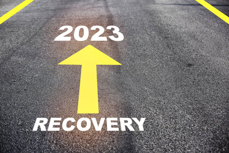 Recovery 2023 with yellow arrow marking on road surface. Business success with direction concept and intelligence future ahead ideaの写真素材
