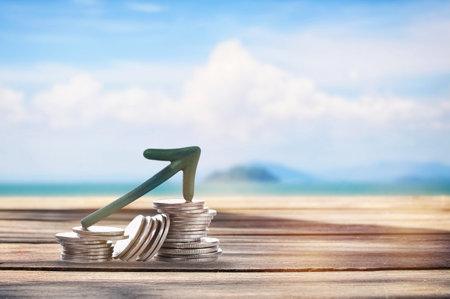 Stack of coins with arrow upwards on planks on tropical beach background. Business beginning with success and return on investment ideaの写真素材