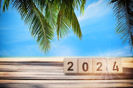 New year 2024 on wooden cube and stack of coins on planks on tropical beach background. Business beginning with success and return on investment ideaの写真素材