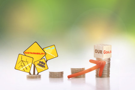 Our goals on cube on stack of coins with environment, society and economics written on yellow sign and arrow upwards on abstract background. Sustainable with return on investment concept and economic growth ideaの写真素材
