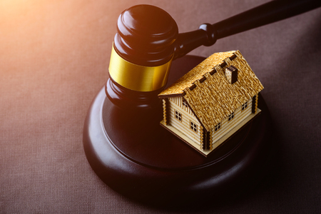 Concept of realty and law. Little wooden house and judges gavel on the table in rays of the sunの写真素材