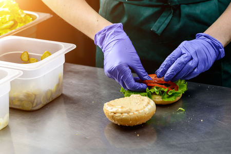 Unidentified chef preparing veggie burger with yummy vegetable patties, tomatoes and lettuce in rays of the sun. Vegetarian food deliveryの写真素材