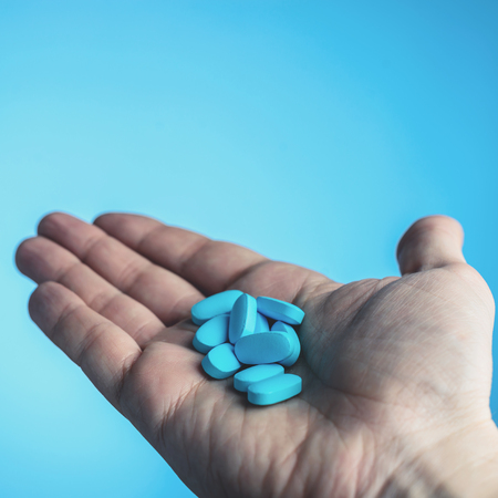 Blue pills in a patiens hands on blue background. Caring for the health concept, toned image