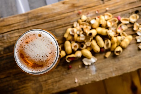 Beer glass with dark cold beer with bubble froth and peanuts onの写真素材