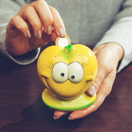 woman putting coins in a funny yellow moneybox, toned image. Concept of future, business, saving money, economy and investmentの写真素材