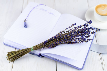 Purple notebook, cup of coffee and flowers on light wooden backgの写真素材