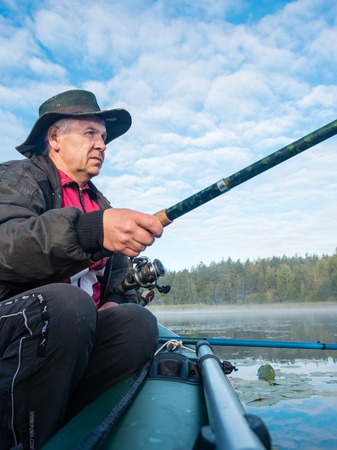 Caucasian fisherman trying to catch fish on a lake at sunny dayの写真素材