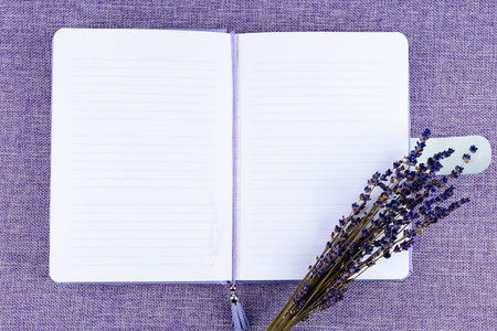 Purple notebook and flowers on purple background with copyspace,