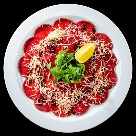 Beef carpaccio with rocket salad, parmesan cheese and lemon in a white plate isolated on black background. Top view, flat layの写真素材