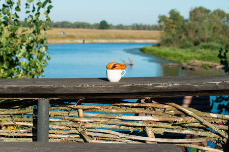 Morning breakfast croissant and a cup of coffee on a background of river landscapeの写真素材