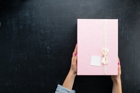 female hands holding a box in the square shape with a present on dark background, flat lay. For Valentines Day, Mothers Day and Birthdays, copy space for textの写真素材