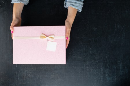 female hands holding a box in the square shape with a present on dark background, flat lay. For Valentines Day, Mothers Day and Birthdays, copy space for textの写真素材