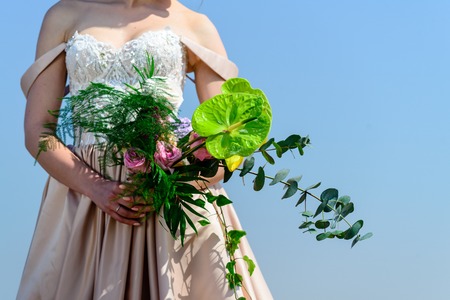 Unidentified bride in beautiful wedding dress holding gentle nice bridal bouquet with fresh blooming flowers, outdoorsの写真素材