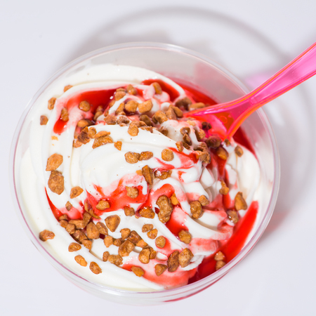 delicious strawberry sundae with nuts in a plastic cup with pink plastic spoon on white surface, flat lay, top viewの写真素材