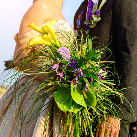 Unidentified young wedding couple. Stylish bride and groom standing with brides bouquet outside on summer dayの写真素材