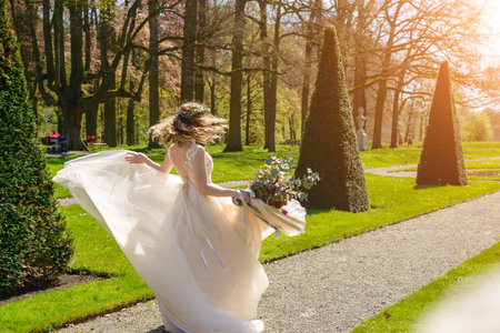 Beautiful blonde happy bride dancing and spinning in the park in her wedding day