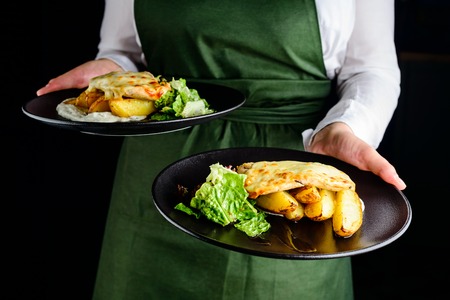 Waiter carrying dishes with potatoes and juicy meatの写真素材