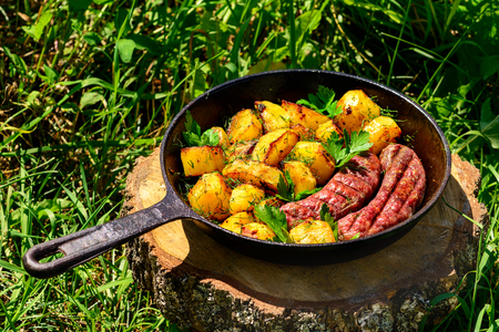 fried beef sausages and delicious yellow potatoes in a frying pan on green grass, lifestyleの写真素材