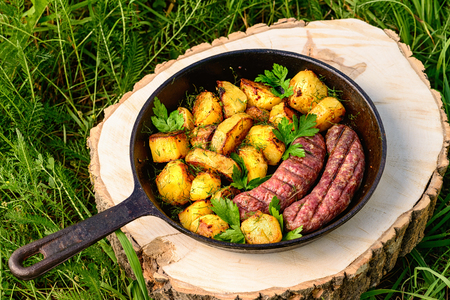 fried beef sausages and delicious yellow potatoes in a frying pan on green grass, lifestyleの写真素材