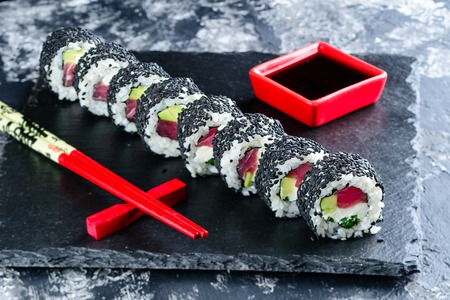 sushi roll with black sesame and tuna, sushi rolls on black tray with soy and chopsticksの写真素材