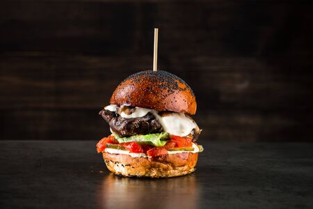 Big tasty hamburger or cheeseburger on black background with grilled meat, cheese, tomato, bacon, onion. Burger closeupの写真素材