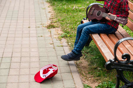 hipie boy play guitar sitting on the sidewalk, boy plays guitar for donation money in a lying hat, street musicianの写真素材