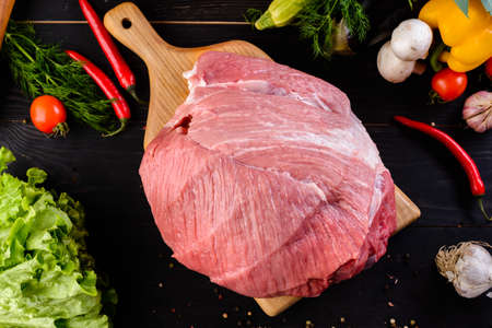 A large piece raw pork meat part of the hip, hip or tenderloin on a black wood background with vegetables and spices, copy space text top view, flat layの写真素材