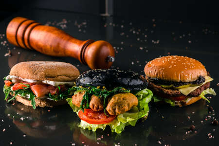 Three burgers with different bread buns on dark background, different new burgers against black background for copy spaceの写真素材