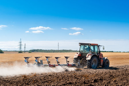 Close-up of agriculture red tractor cultivating field over blue sky, Plowing in the fields