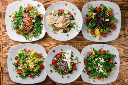 Set of plates with vegetable salad. Healthy food for dieting. Lunch menu of food restaurant in rustic style, top view set of six salads on a wooden tableの写真素材