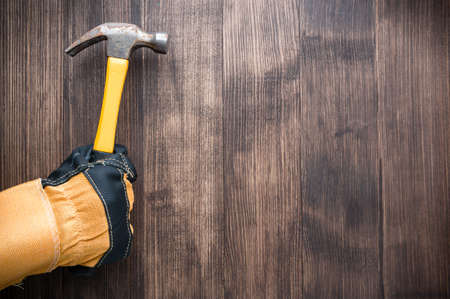Top view of a hand protected by leather work gloves hold hammer on wooden table. worker's hand in a construction glove holds a hammer top view, copy spaceの写真素材