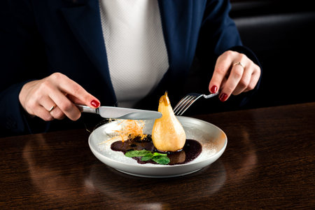 Female hands cuts caramel pears over dark table, woman eats dessert caramelized pear with chocolate