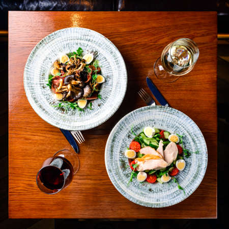 two salads and two glasses of wine on the table top view, Restaurant table set up for two main dish fine dinning white wine glass on wooden tableの写真素材