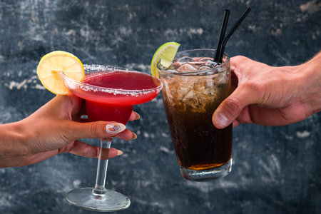 Red margarita cocktail and Rum and Cola Cuba Libre cocktail in a womans handの写真素材