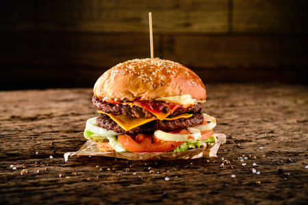 Close-up of a tasty double hamburger with cheese and deep fried ground meat on a wooden tableの写真素材