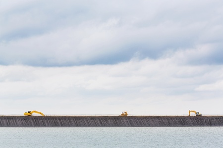 Yellow color backhoes working on dam crest の写真素材